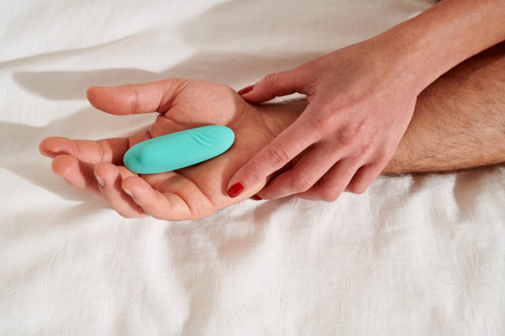 Mão masculina segurando um vibrador para casal azul, enquanto uma mão feminina segura ela também