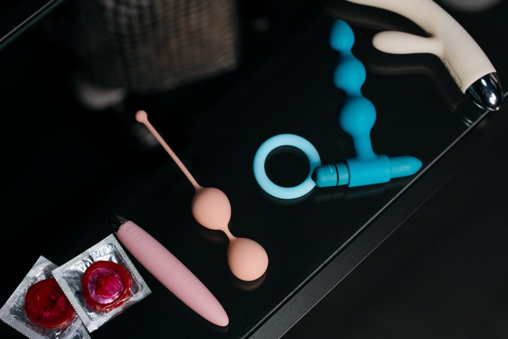 Mesa preta com produtos em cima dela: preservativos, tipos de vibradores e um anel peniano