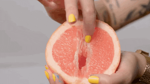 Uma mão segurando uma laranja enquanto a outra mão passa no meio da laranja com o dedo indicador, remetendo a masturbação