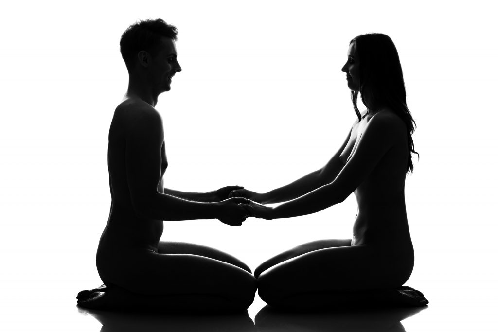 Homem e mulher sentados de joelho, olhando um para o outro e dando as mãos, porém aparece somente a sombra deles.