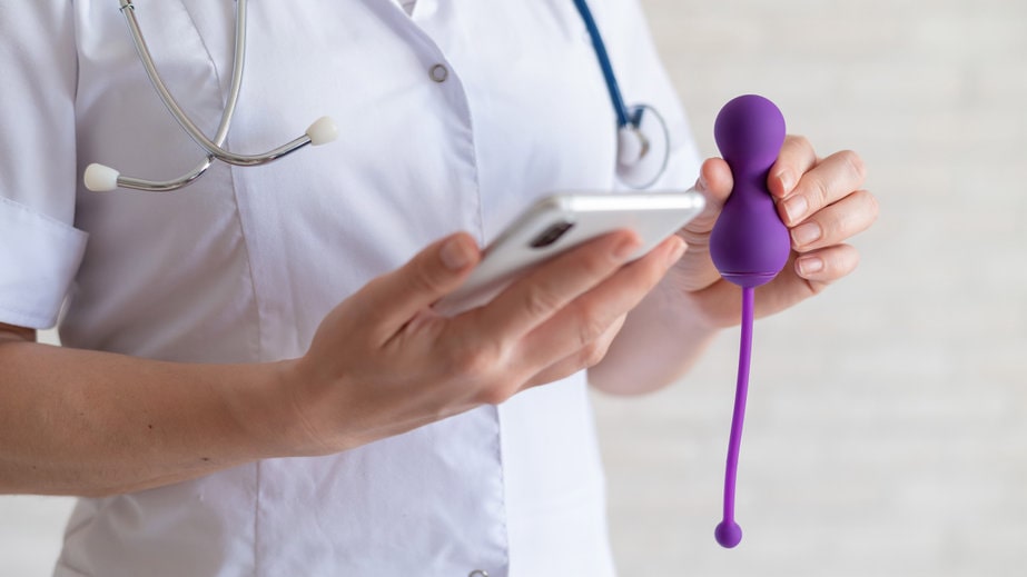 médica com jaleco segurando um celular na mão esquerda e um produto de pompoarismo na mão direita