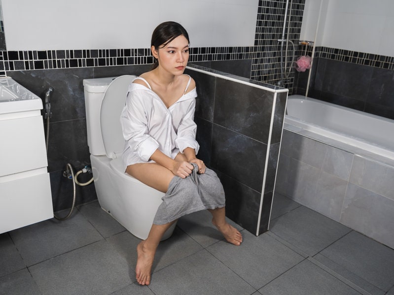 Mulher sentada na privada segurando o shorts com cara de preocupação devido ao corrimento vaginal