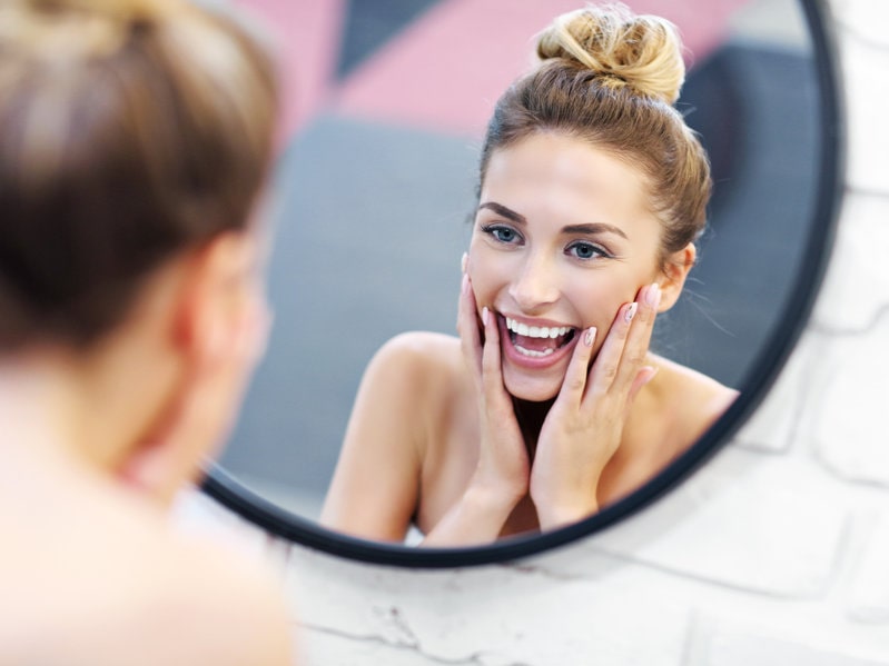mulher feliz se olhando no espelho representando a autoestima, um dos benefícios da masturbação