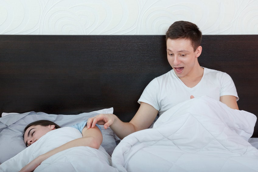 mulher dormindo e homem ao lado dela com o edredom levantado, olhando seu orgão sexual com cara de surpresa