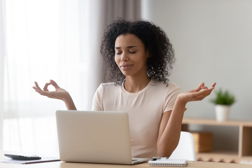 Mulher negra meditando na frente do notebook representando um dos benefícios de transar menstruada, que é o alívio de cólicas e melhora do humor