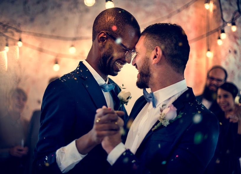 Orgulho lgbtqia+: dois homens se casando de terno sorrindo um para o outro
