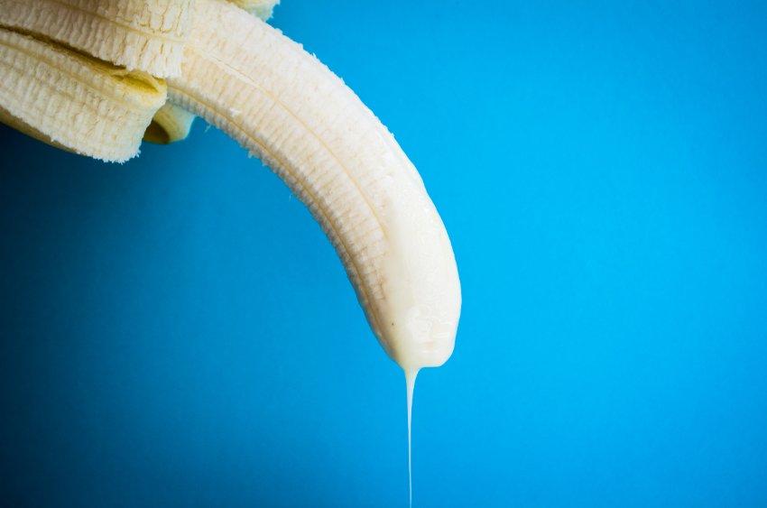 Banana apontada pra baixo com líquido branco na ponta em um fundo azul