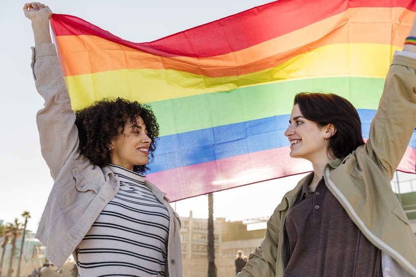 duas mulheres segurando uma bandeira colorida que remete ao orgulho lgbtqia+
