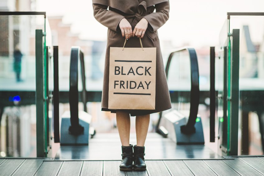 Mulher na frente da escada rolante com uma sacola escrito Black Friday