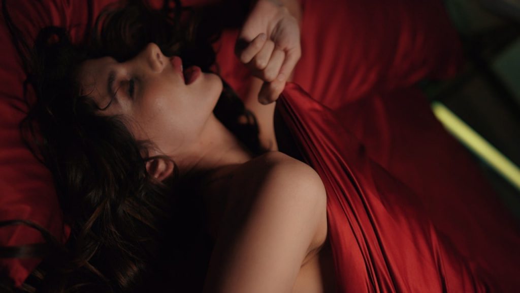 mulher de olho fechado, deitada com lençol vermelho apimentando a relação