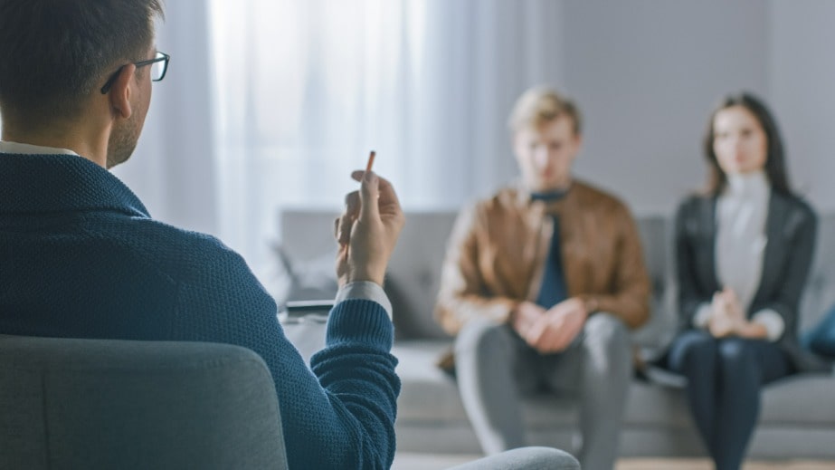 Terapia de casal - Homem e mulher sentados no sofá enquanto o terapeuta está olhando e anotando