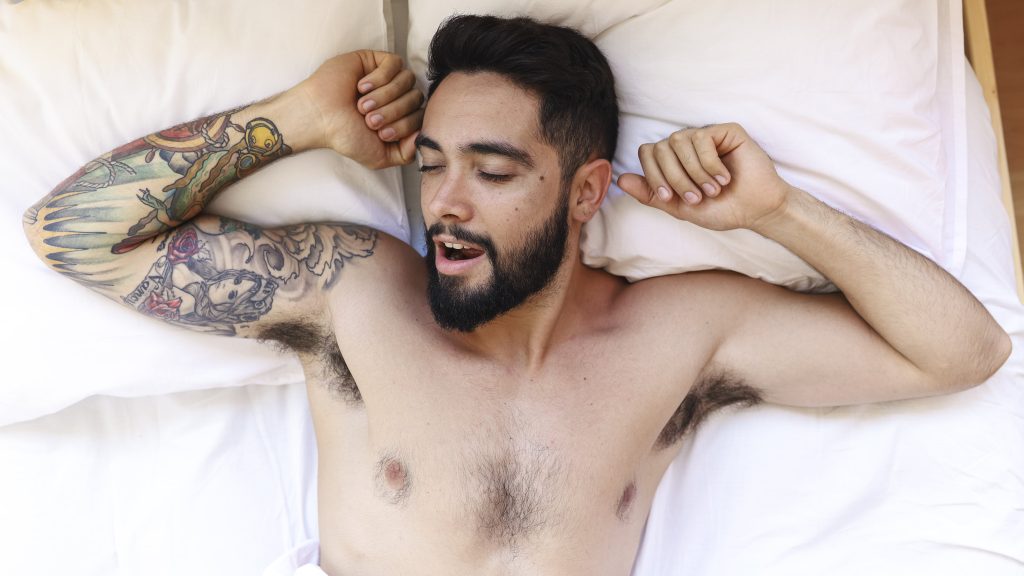 Homem sem blusa deitado na cama, com cara de prazer por estimular o Ponto G masculino
